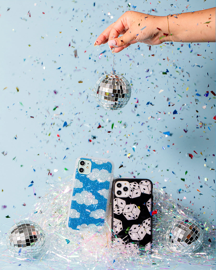 Front view of two iPhone cases with glitter blue cloud and black dice prints, confetti and disco balls on pale blue background