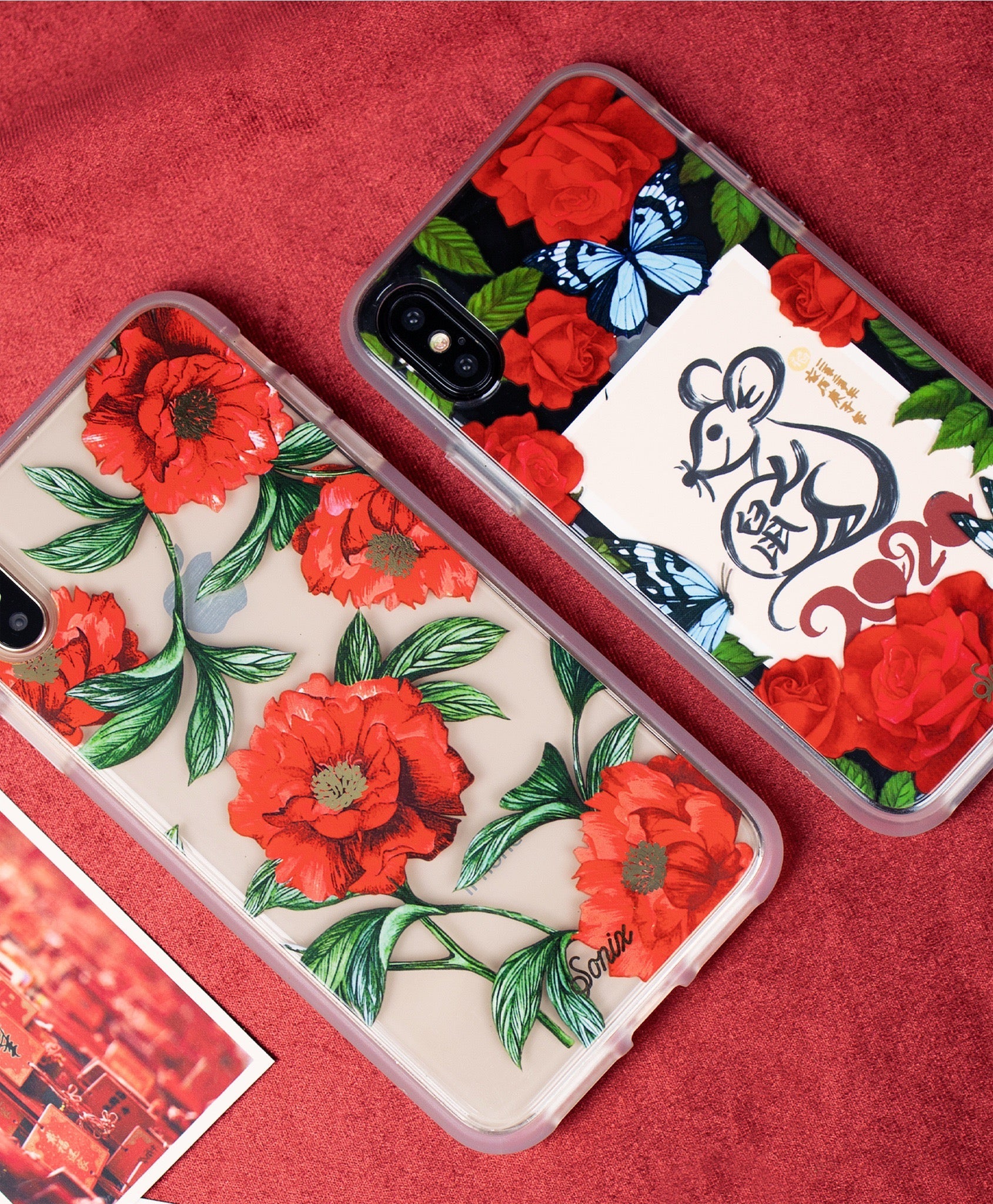 Angled flat lay of two iPhone cases showcasing red floral print and Lunar New Year rat design on a red fabric background