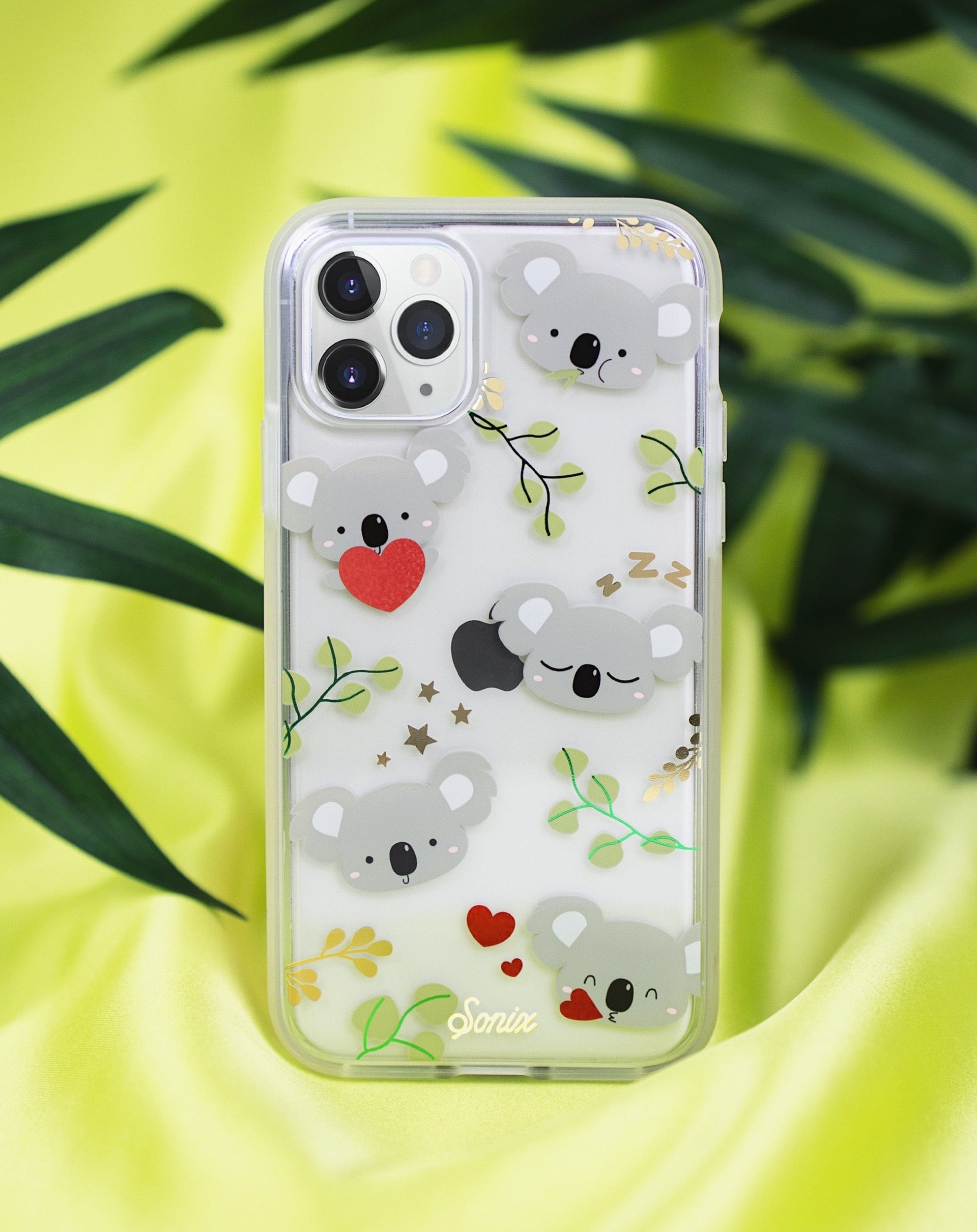 Close-up of Koala Love iPhone case with gray koalas, red hearts, green leaves and gold foil on lime-green background
