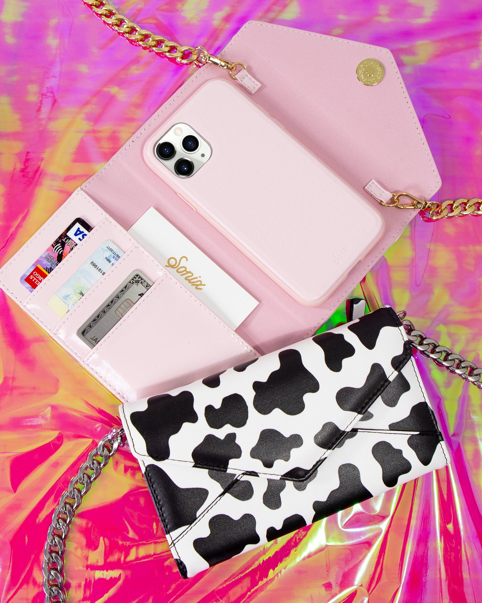 Top-down view of blush pink crossbody phone case with chain strap, card slots and iPhone on iridescent pink background