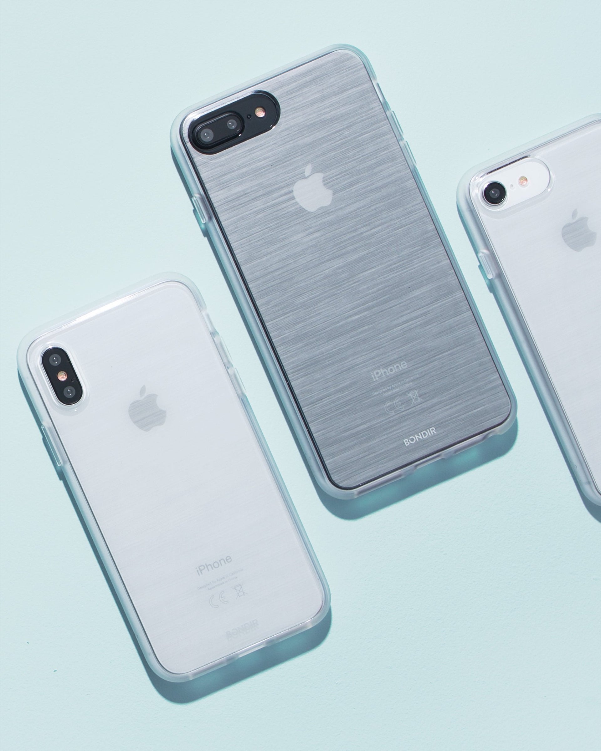 angled top-down view of Bondir iPhone cases showing clear protective bumpers and a brushed-metal back on a pale blue background