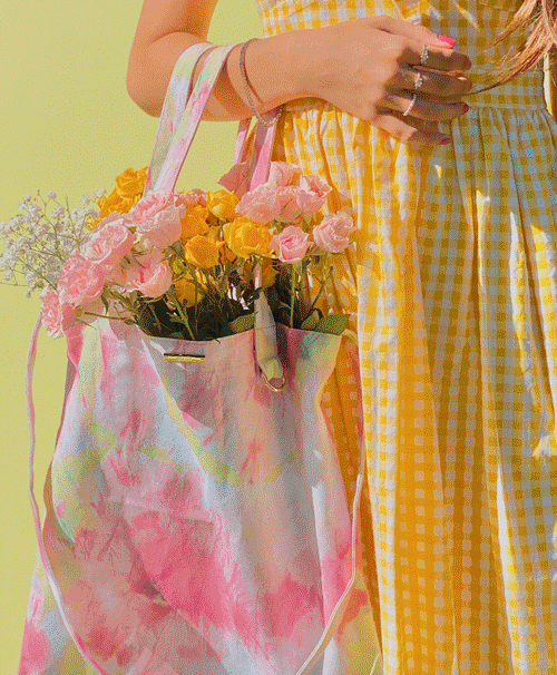 Woman holding a pastel tie-dye tote bag filled with pink and yellow roses against a pale green background