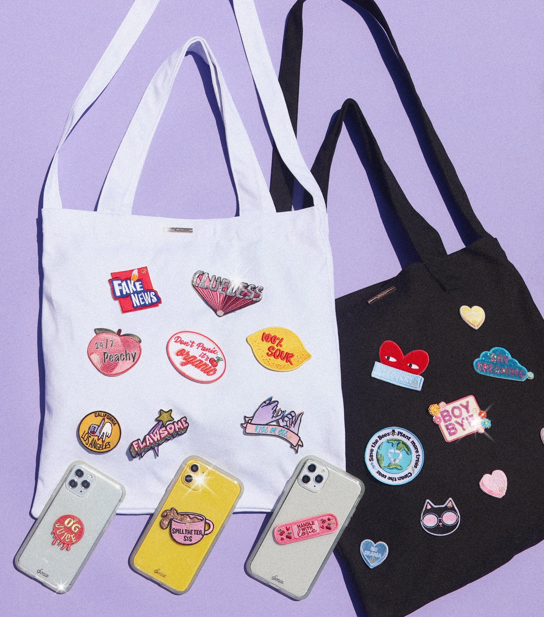 Top-down view of white and black tote bags and three iPhone cases showcasing colorful self-adhesive patches on a lavender background