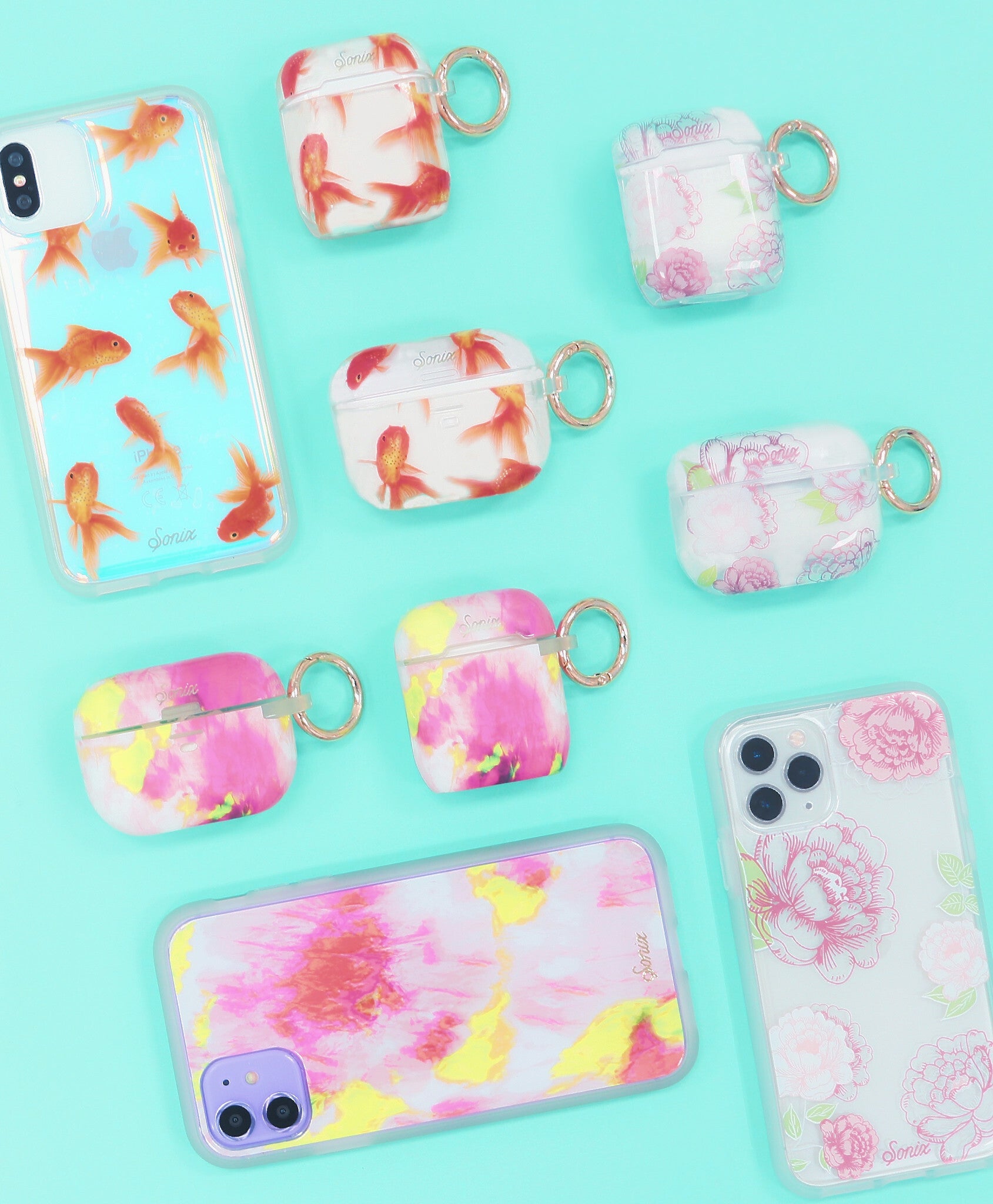 Flat lay of AirPods cases with colorful prints (goldfish, floral, pink) and rose-gold key rings on turquoise background