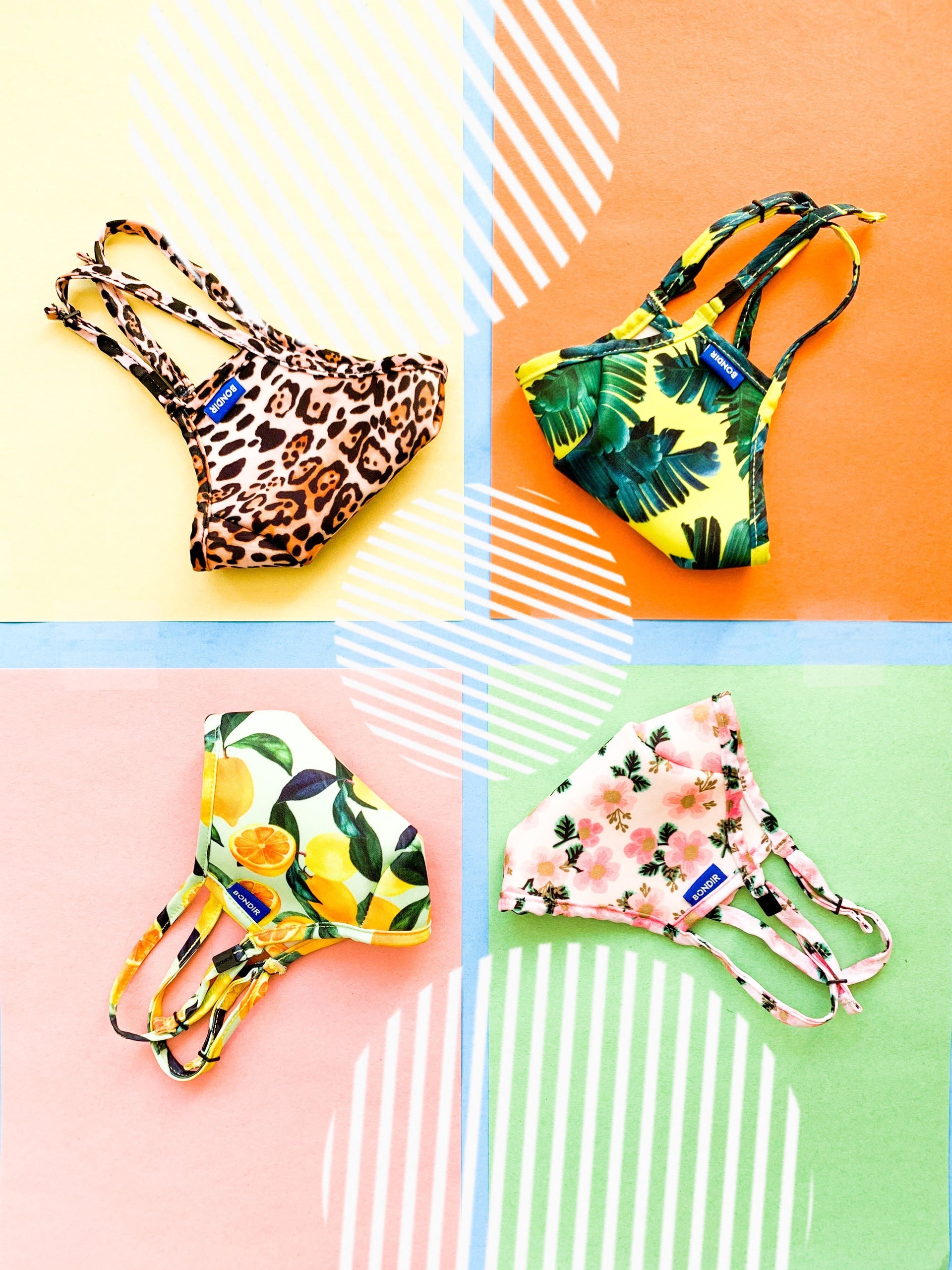 Flat lay of four Bondir Air Guard face masks in leopard, tropical leaf, lemon, floral prints on a pastel quadrant background