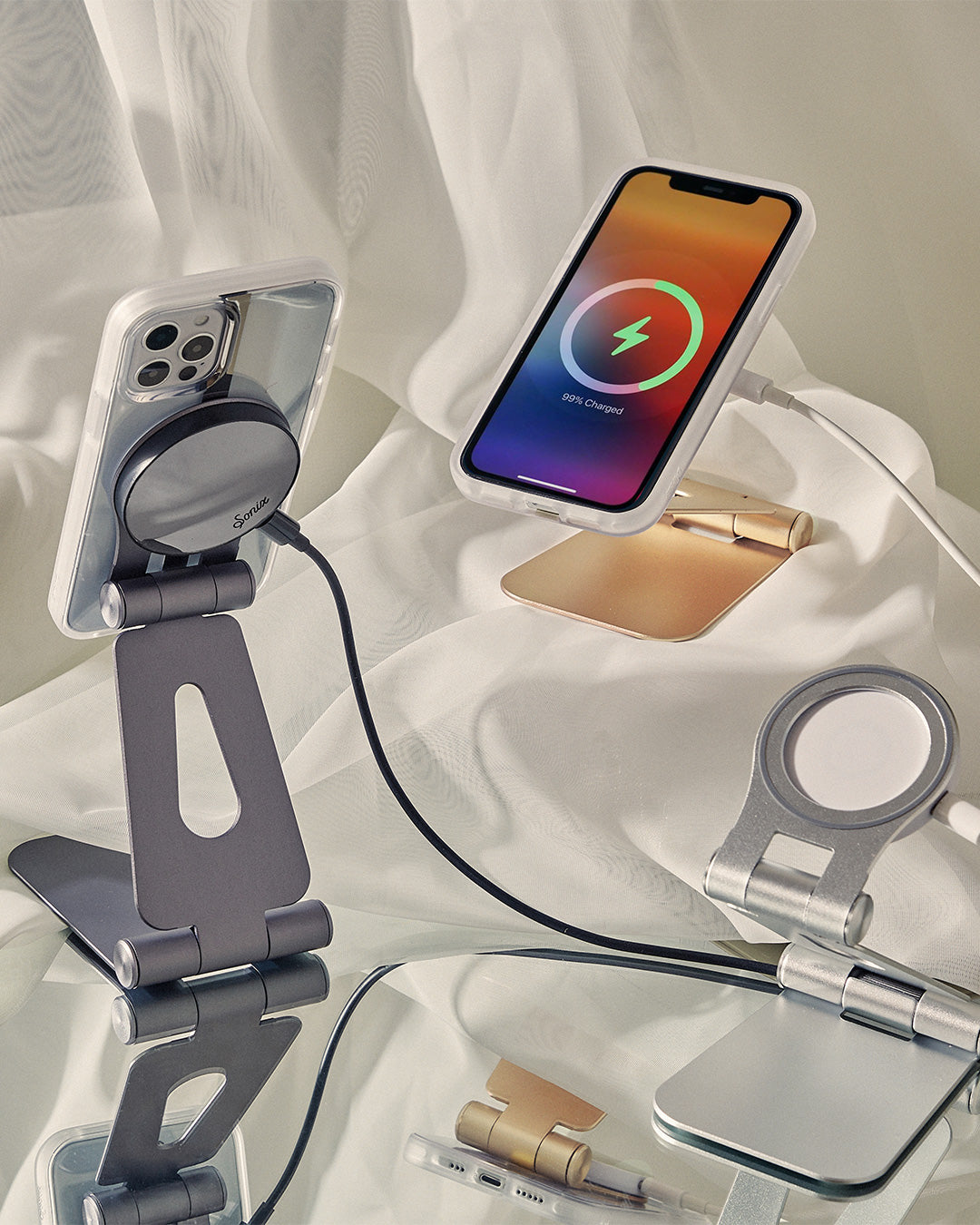 Two iPhones charging on Sonix magnetic chargers and adjustable phone stands on a draped fabric backdrop
