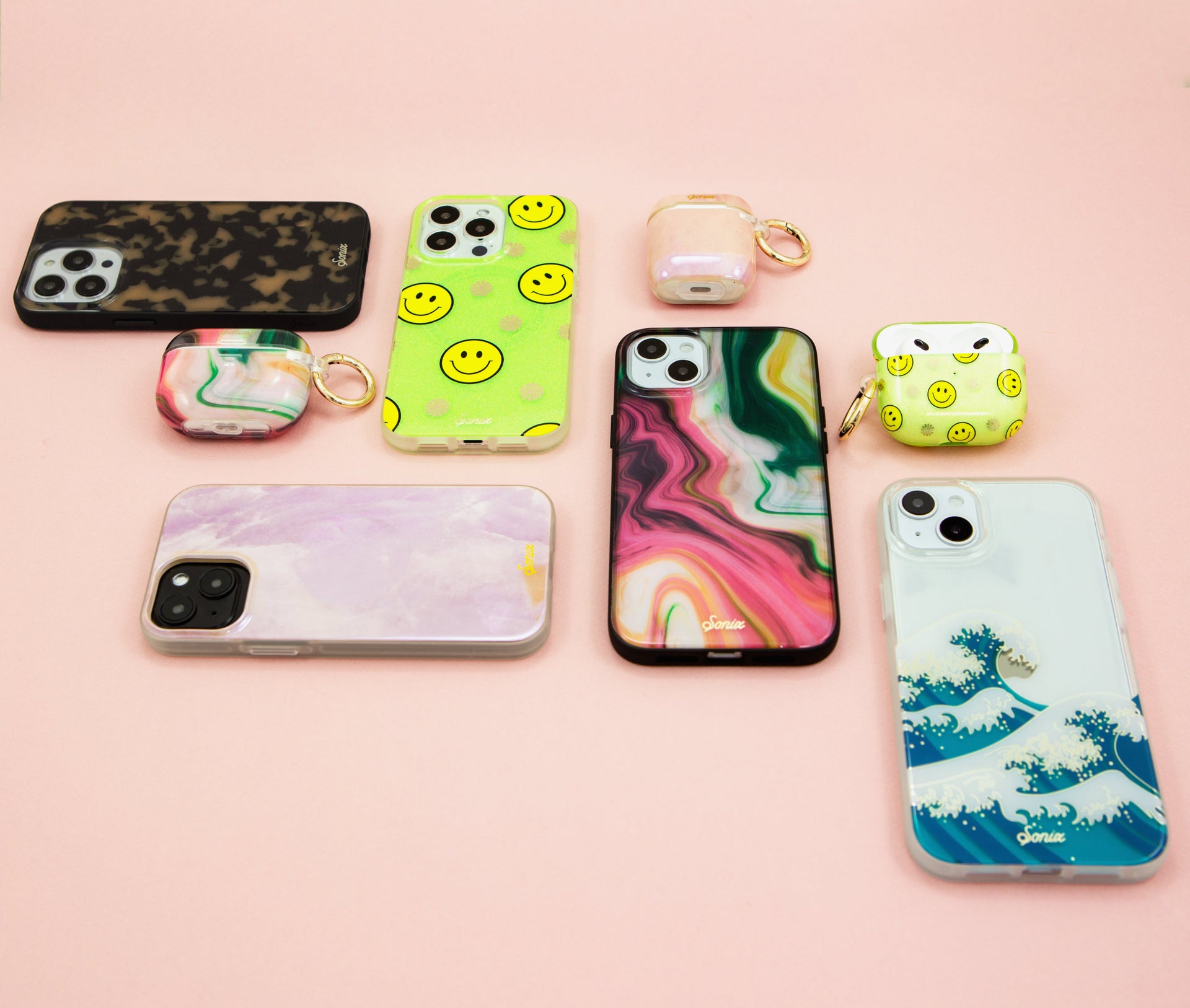 Overhead flat lay of iPhone and AirPods Cases showing neon smiley, marbled, purple marble, and wave designs on pink background