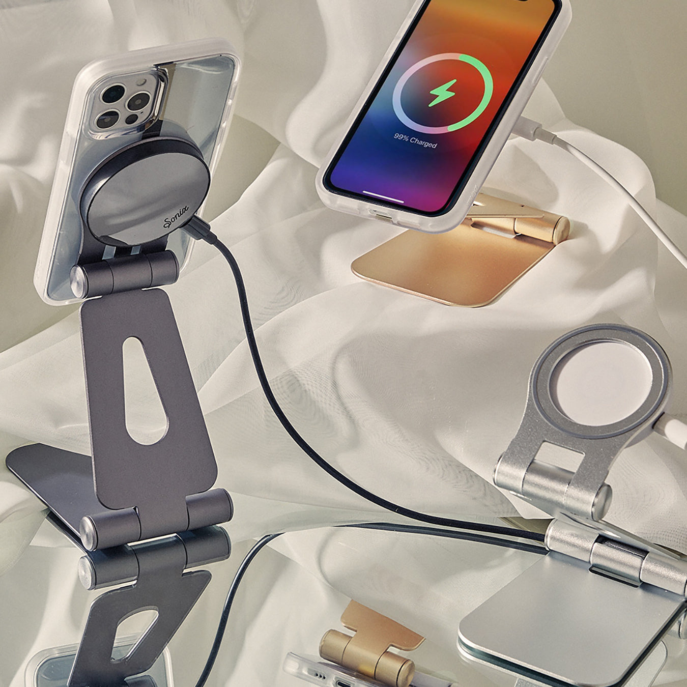 Two iPhones charging on adjustable metal stands with magnetic wireless chargers on a reflective fabric backdrop