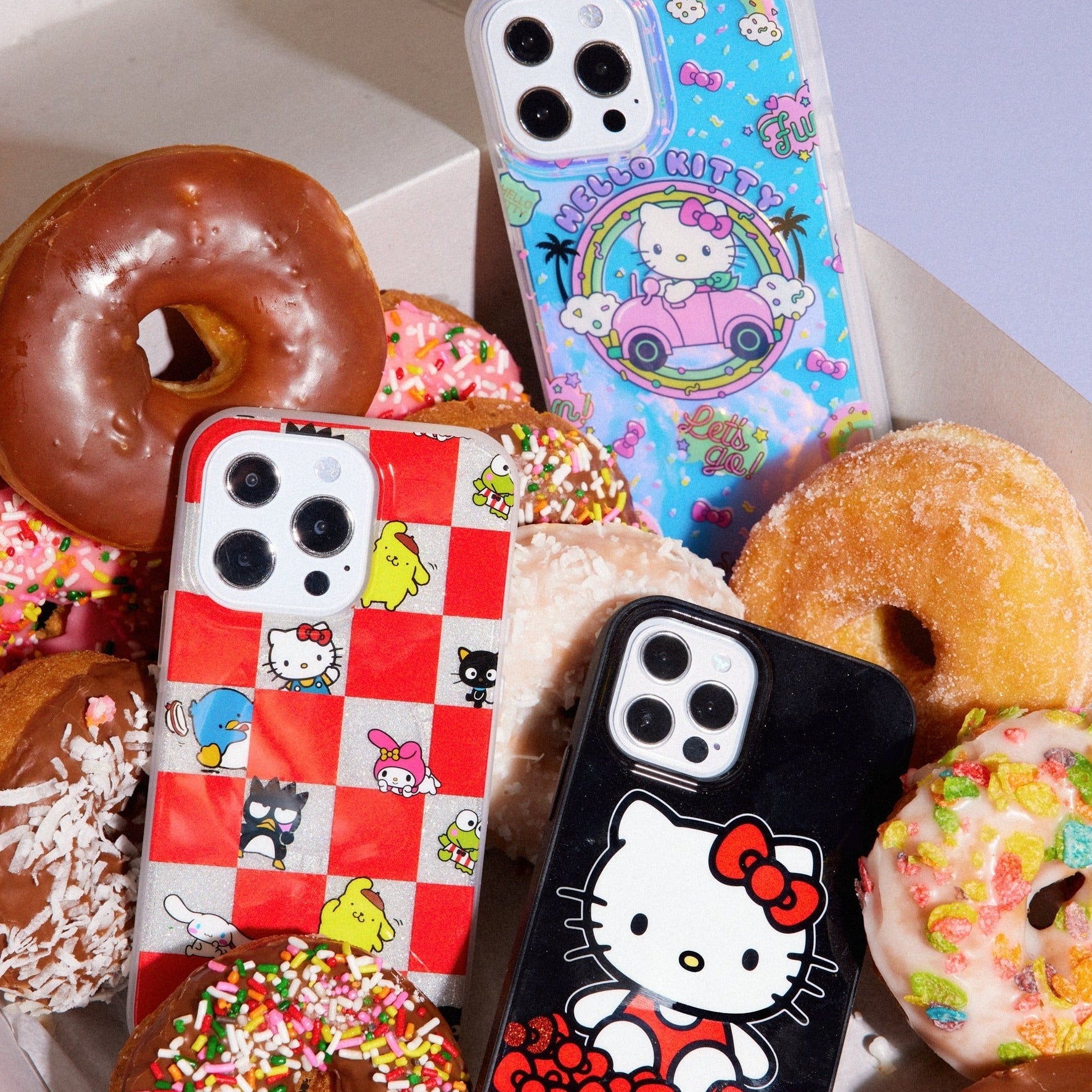 three hello kitty themed phone cases shown in a box of donuts