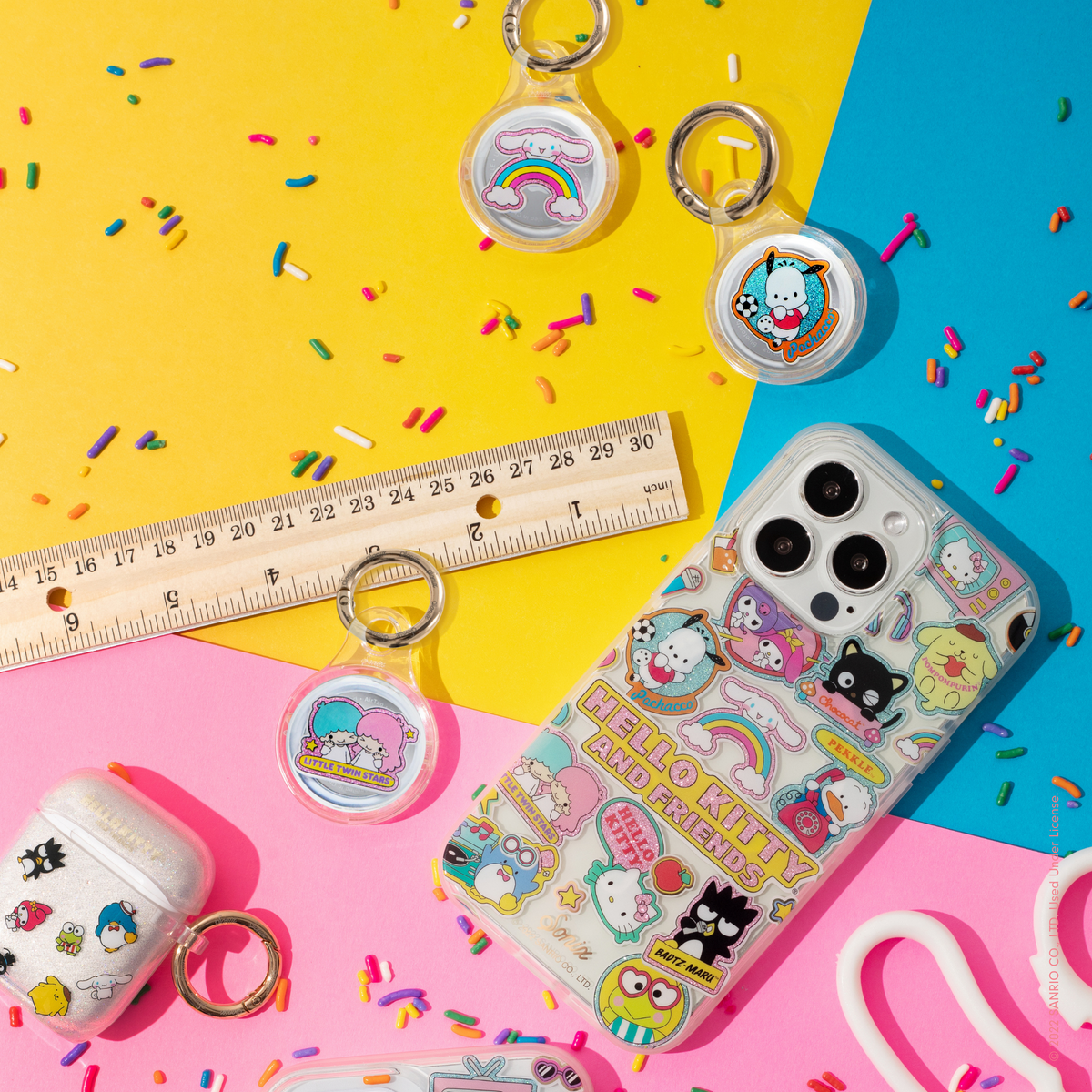 clear case with many beloved hello kitty characters featuring multi-color glitter and classic gold foiling shown on an iphone 12, airpod case, and airtag case