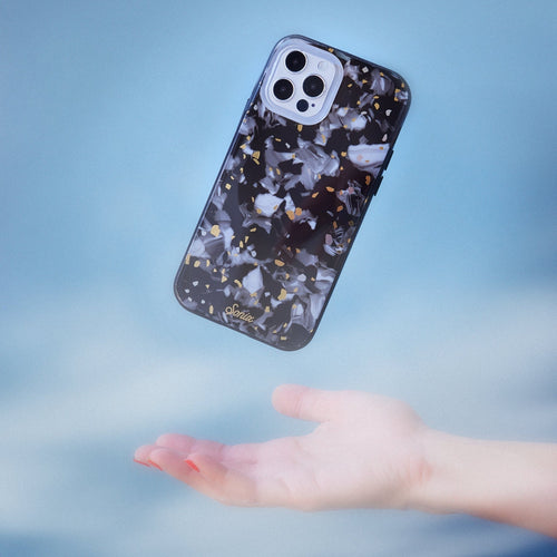 Dark galaxy rocks with highlights of gold and white on a black base.case shown on an iphone 12 with a blurred blue background