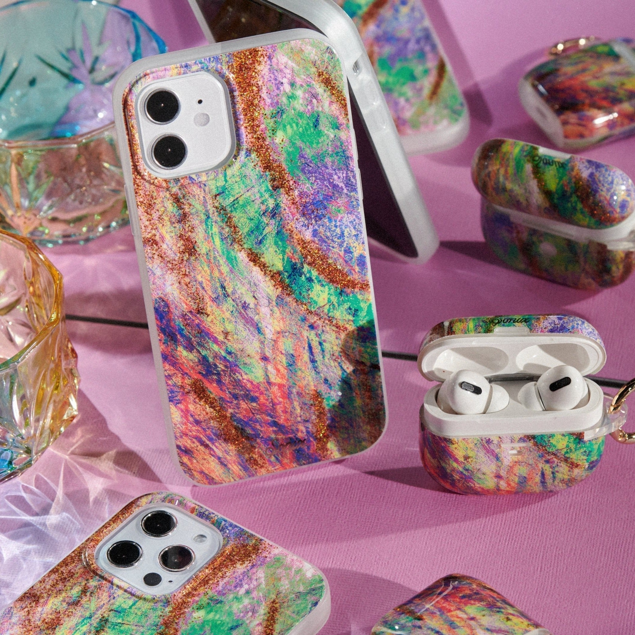  a paint splash of colors, resembling the Mardi Gras carnival, and finished with accents of gold glitter shown on an iphone and airpods pro 