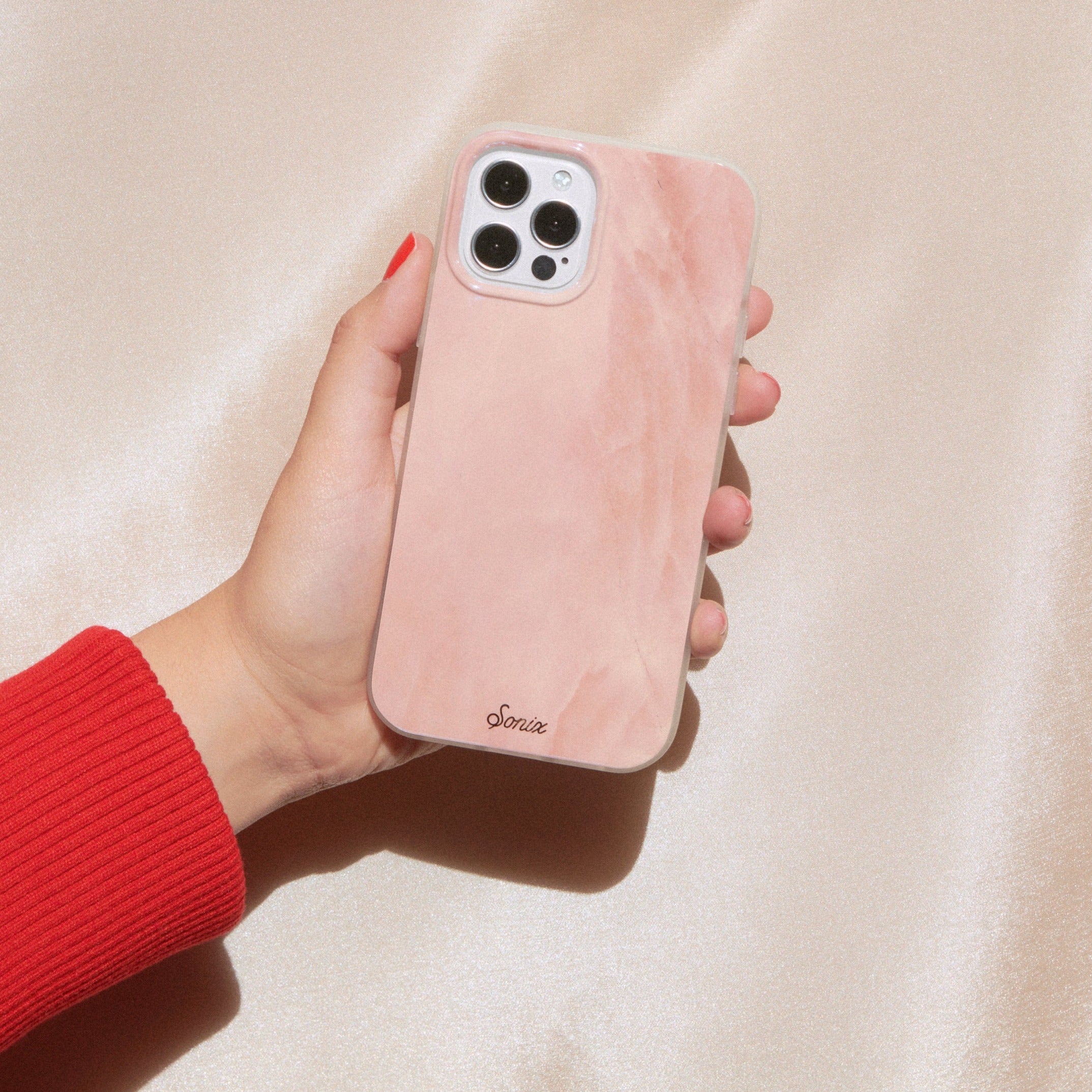 a gleaming pearl design with a pink finish shown on an iphone 12 being held by a hand with a pink background